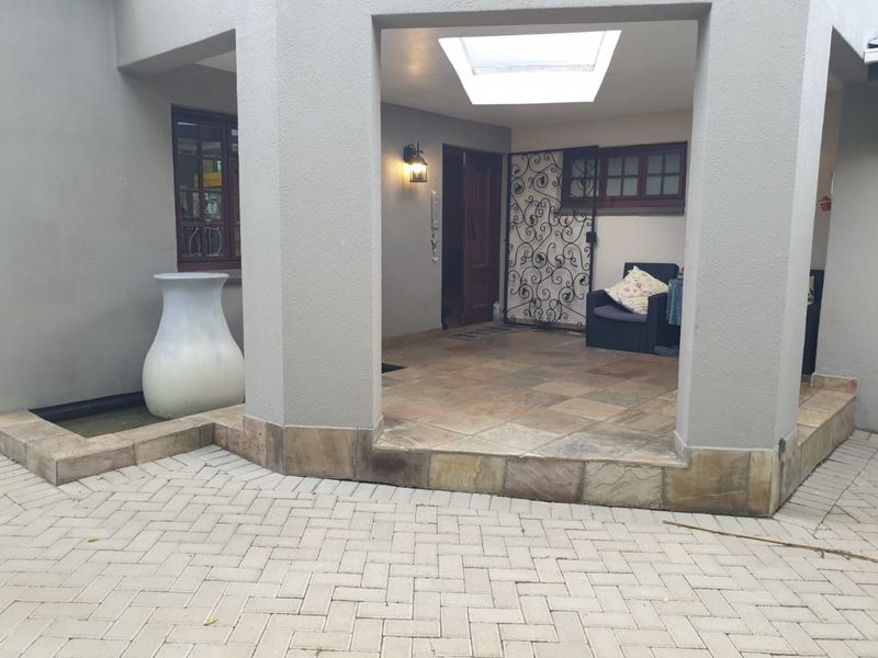 A covered patio entrance area featuring stone tile flooring, a skylight, and a decorative wrought iron security gate.