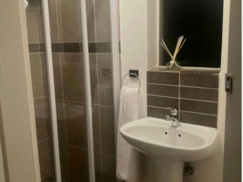 A compact bathroom featuring a pedestal basin, tiled splashback, and a glass-enclosed shower unit with neutral wall tiling.