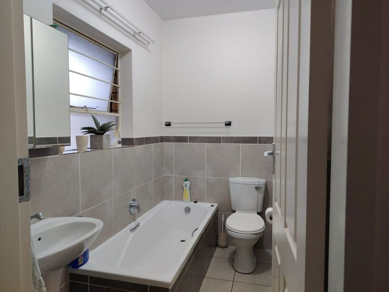 A functional bathroom featuring a pedestal basin, built-in bathtub, and toilet with neutral wall and floor tiling.