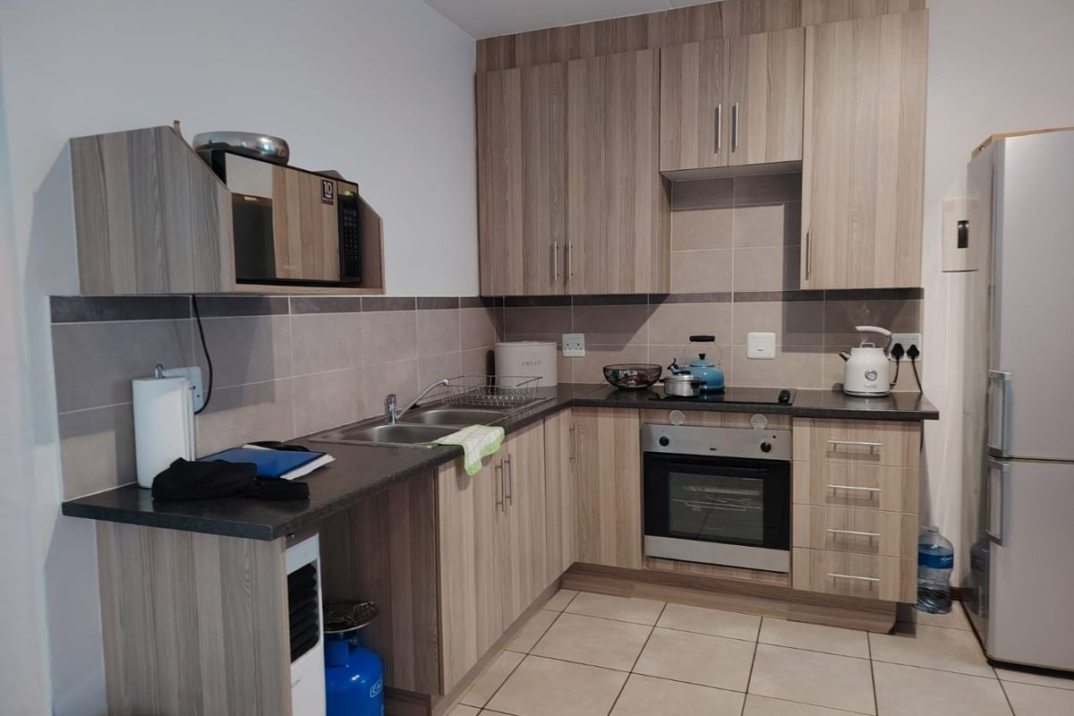 A functional kitchen featuring wood-look cabinetry, dark laminate countertops, a built-in oven, and a tiled backsplash with neutral floor tiles.
