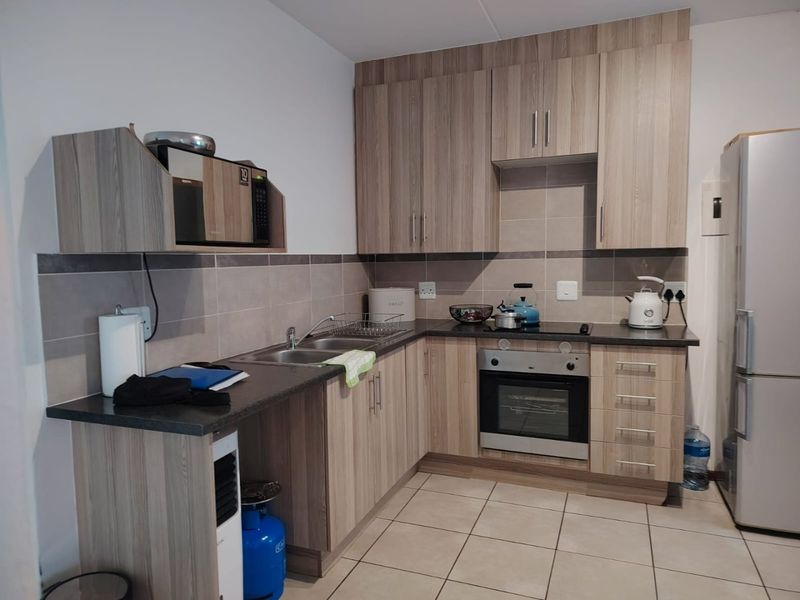 A functional kitchen featuring wood-look cabinetry, dark laminate countertops, a built-in oven, and a tiled backsplash with neutral floor tiles.