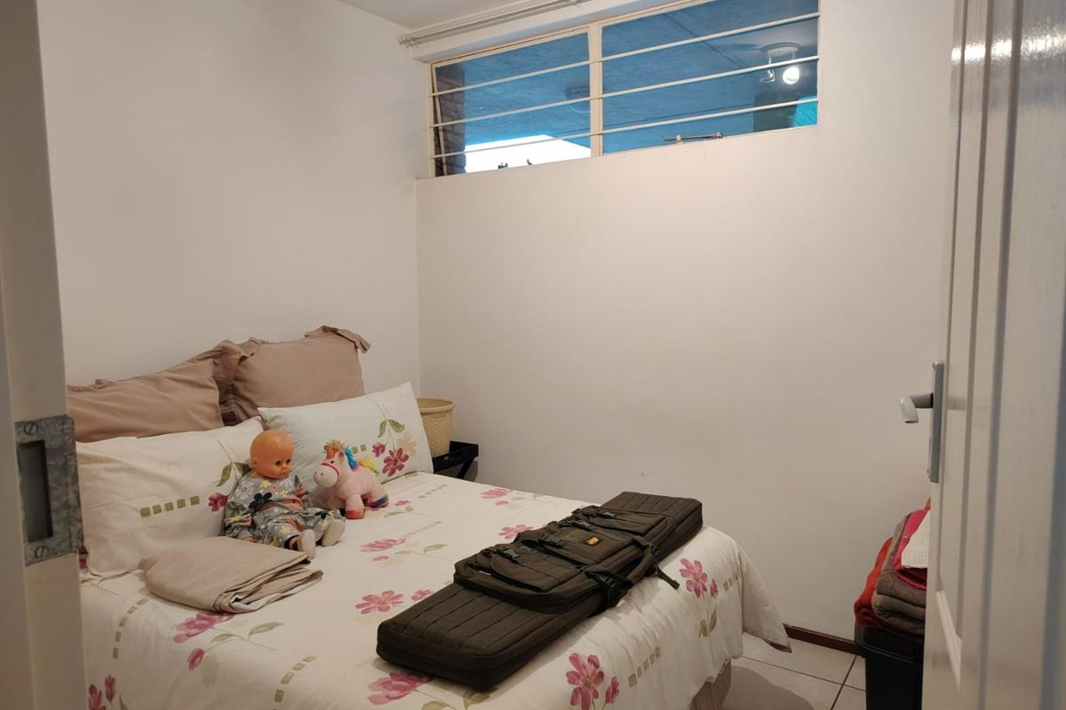 A compact bedroom featuring tiled flooring and a high-set window with security bars, providing a functional and secure living space.