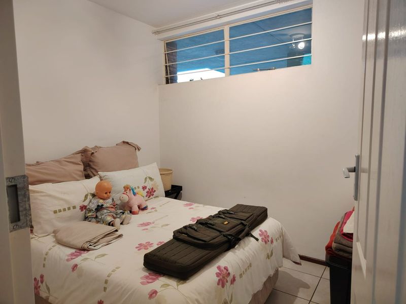 A compact bedroom featuring tiled flooring and a high-set window with security bars, providing a functional and secure living space.