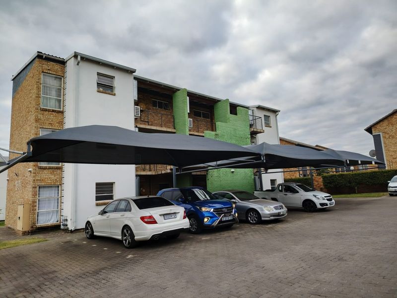 Exterior view of an apartment complex featuring a paved parking area with shade cloth carports and multi-story residential units with balconies.