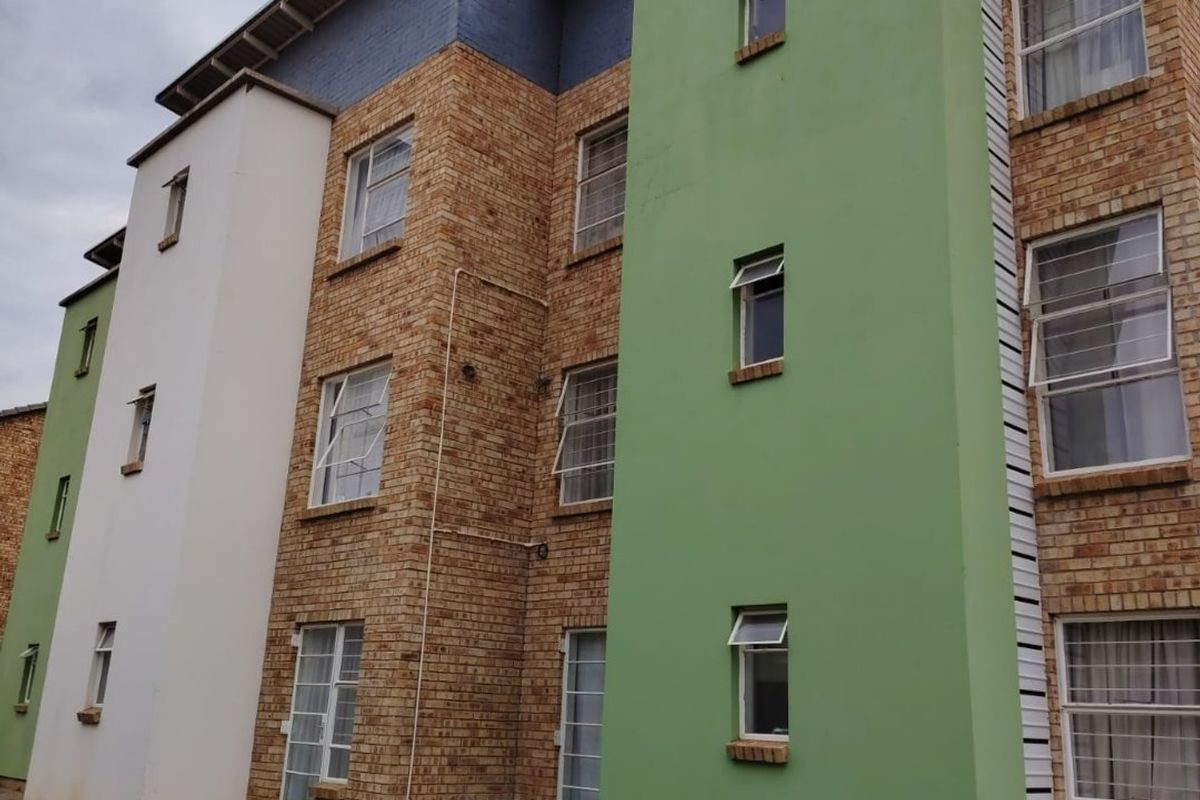 Exterior view of a multi-story apartment building featuring a combination of brickwork, painted plaster sections, and casement windows with a paved ground-level walkway.