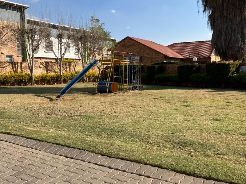 A communal garden area featuring a paved walkway, established lawn, and brick boundary wall within the apartment complex.