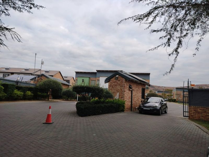 View of the apartment complex entrance featuring a brick guardhouse, paved driveway, and secure perimeter fencing.