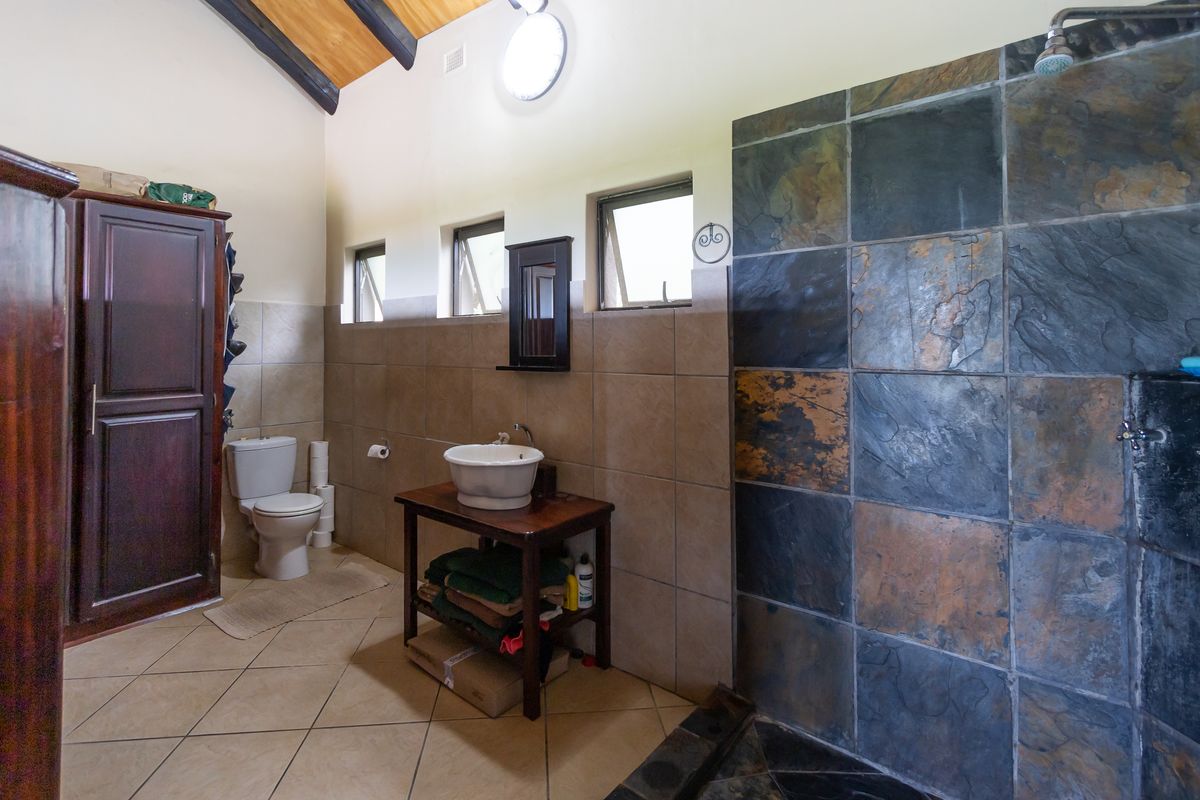 Bathroom featuring a walk-in shower with slate-style tiling, a vessel sink vanity, and a toilet, set under a high vaulted ceiling with exposed beams.