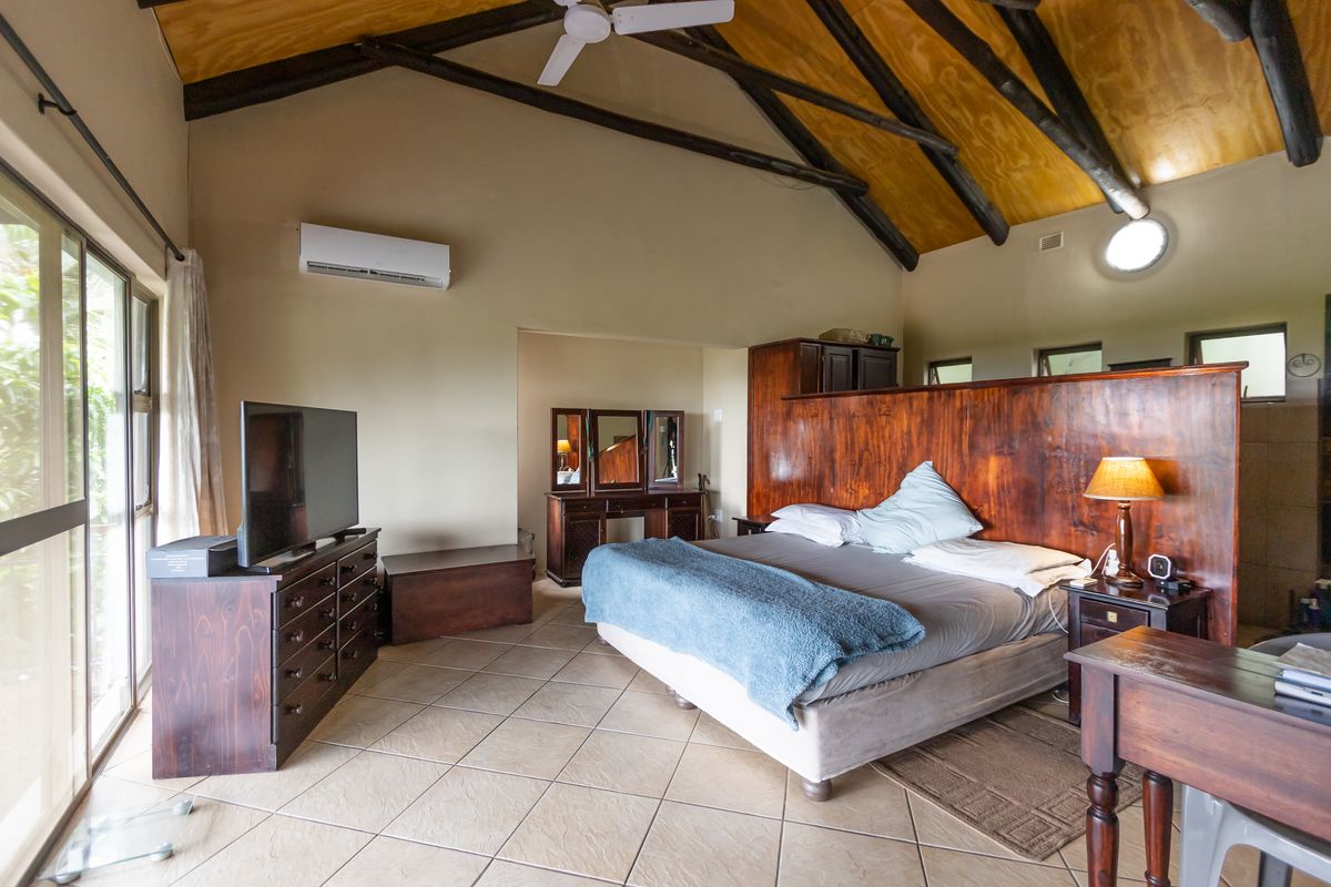 Spacious bedroom featuring a vaulted timber ceiling with exposed beams, tiled flooring, a wall-mounted air conditioning unit, and large sliding glass doors.