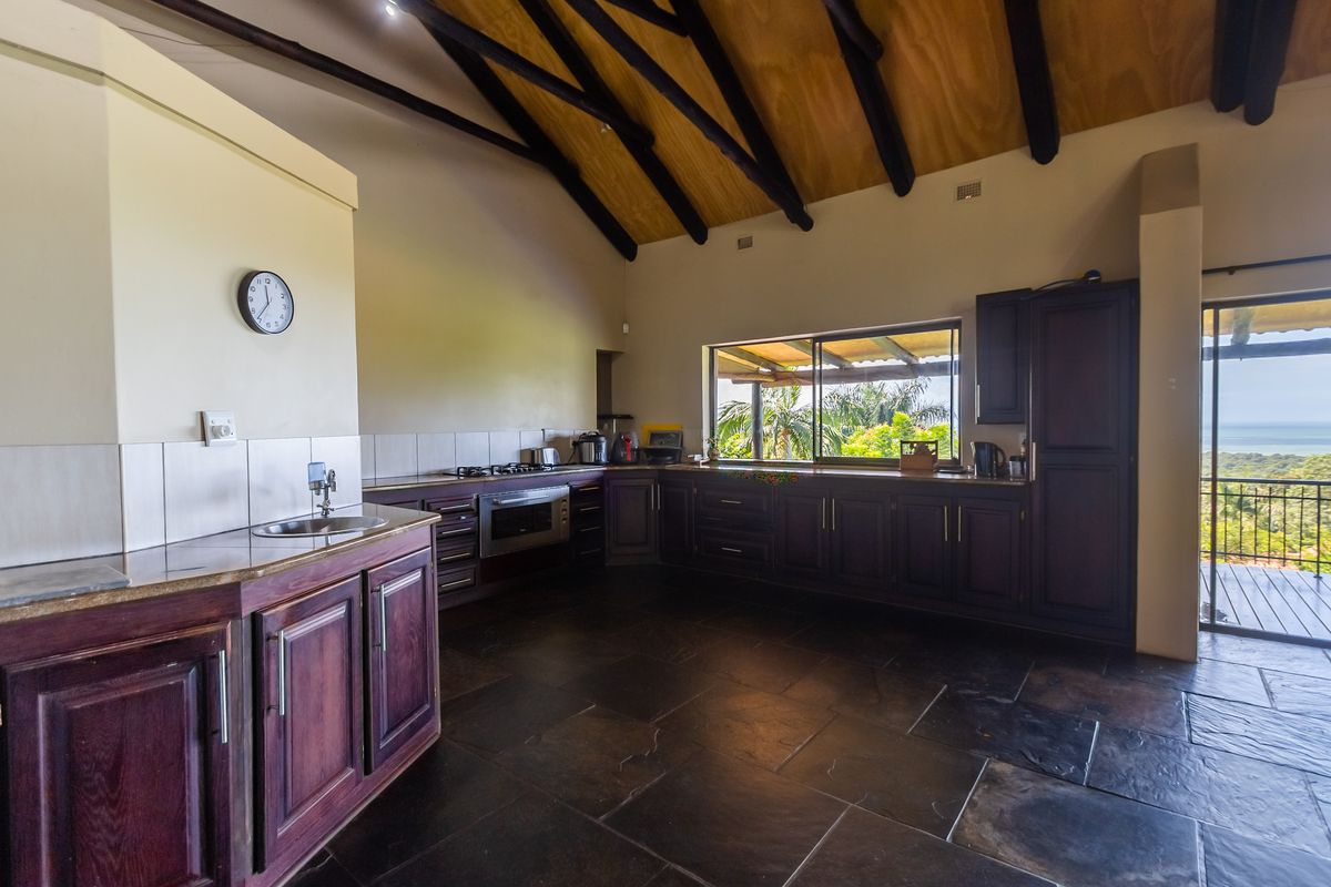 Spacious kitchen featuring dark wood cabinetry, built-in oven and hob, vaulted timber ceiling with exposed beams, and direct access to an outdoor balcony.