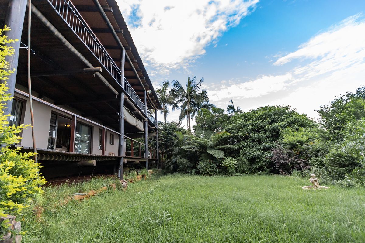 A view of the rear exterior of the house featuring a multi-level timber deck, balcony, and a spacious garden area with mature trees.