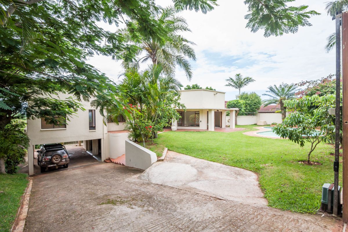 Spacious rear garden featuring a swimming pool, covered patio area, and a concrete driveway leading to an undercover parking space.