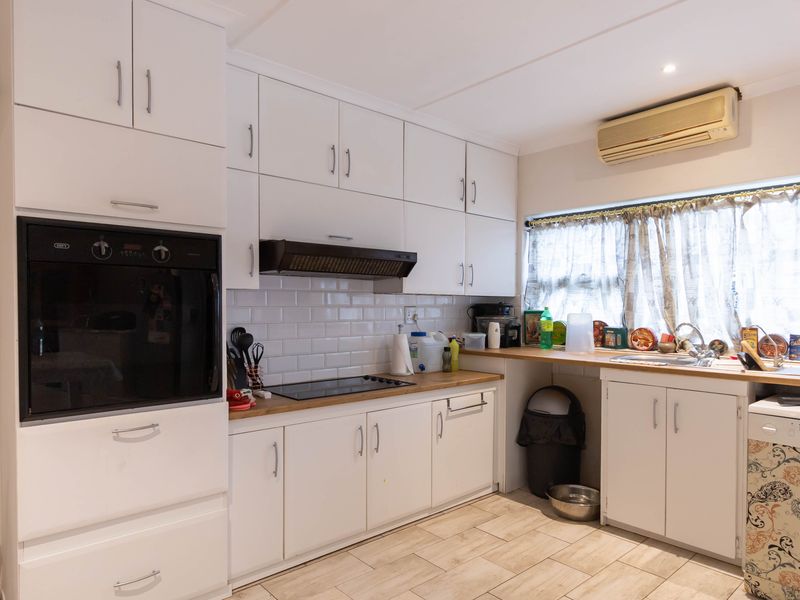 A functional kitchen featuring white cabinetry, wooden countertops, subway tile backsplash, built-in oven, hob, and an integrated air conditioning unit.