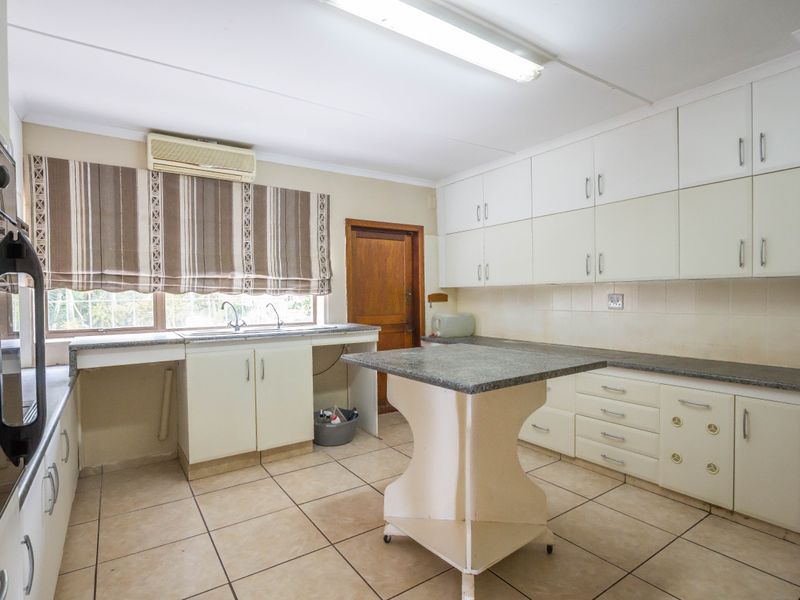 A functional kitchen featuring ample built-in cabinetry, stone countertops, tiled flooring, and a wall-mounted air conditioning unit.