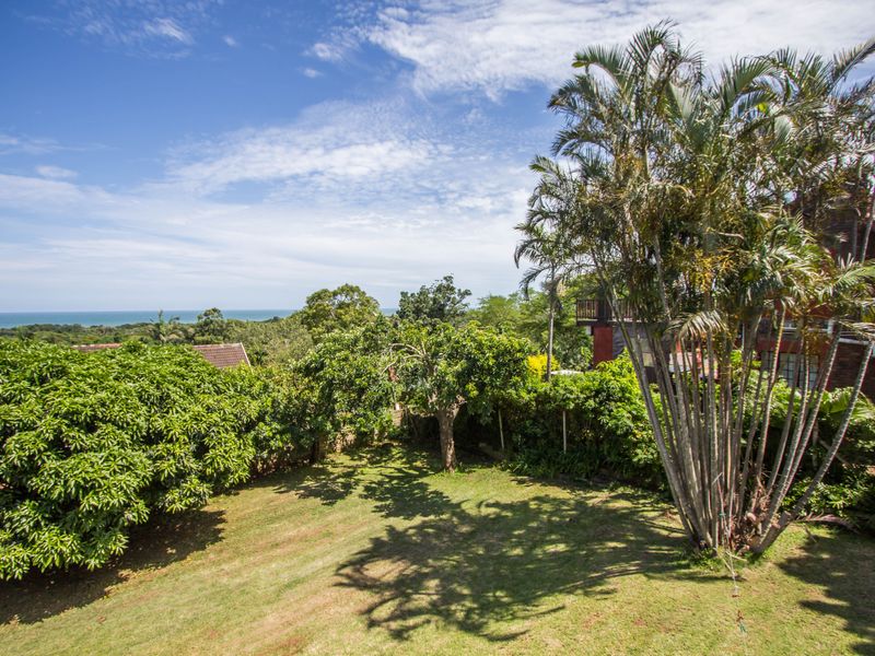 A scenic elevated view overlooking a lush green garden with mature trees and a distant ocean horizon.