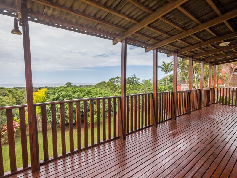 A spacious covered timber balcony featuring a wooden balustrade and exposed rafters, offering elevated views over the surrounding garden and landscape.
