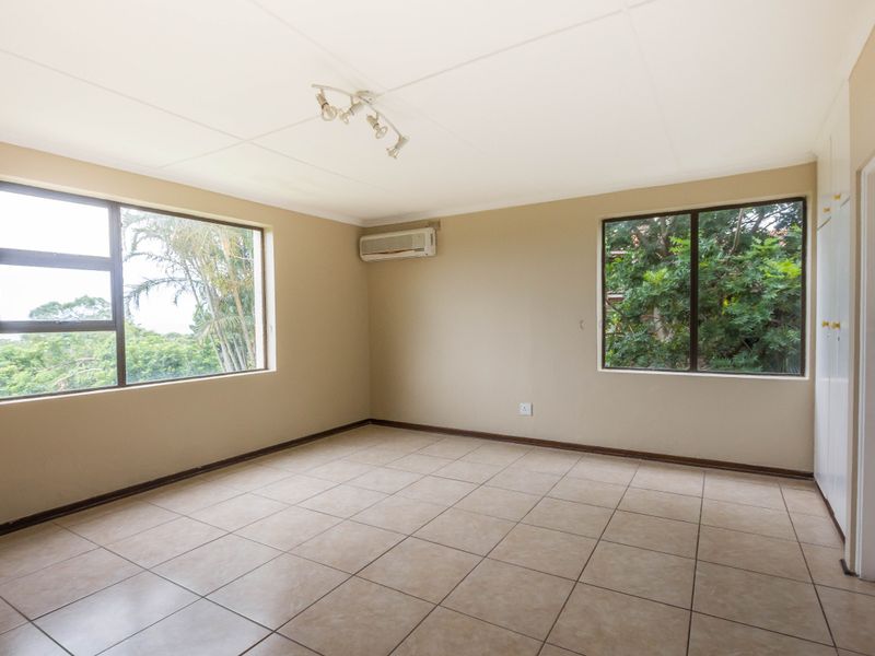 A spacious, empty bedroom featuring neutral tiled flooring, built-in cupboards, and an integrated air conditioning unit, offering a clean canvas for personalization.