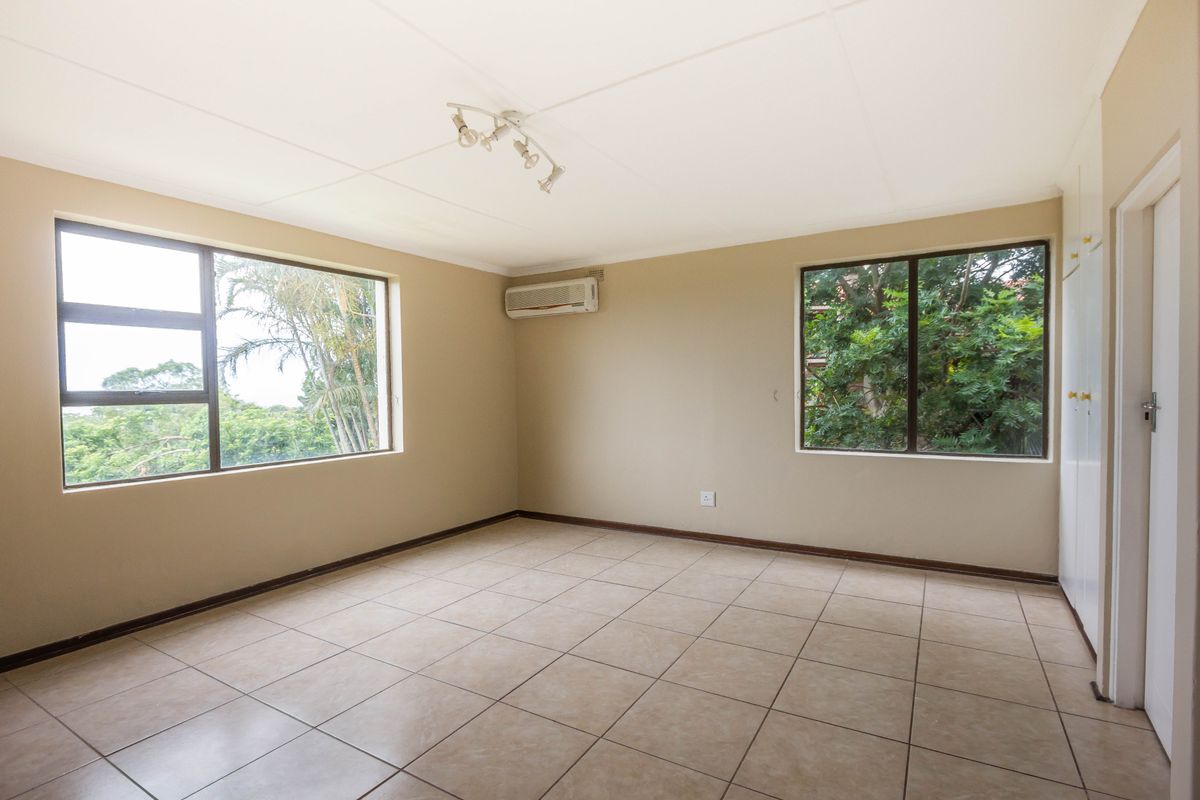 A spacious, empty bedroom featuring neutral tiled flooring, built-in cupboards, and an integrated air conditioning unit, offering a clean canvas for personalization.