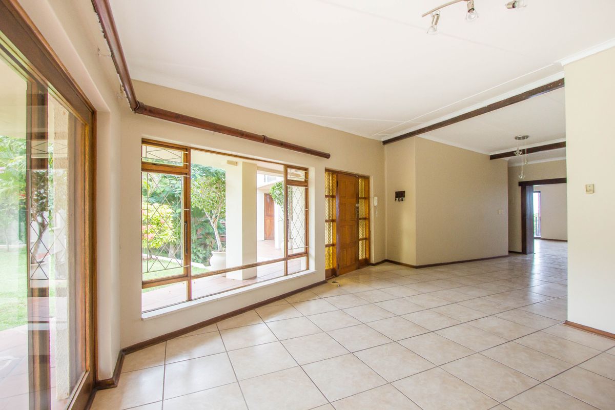 Spacious, empty living area featuring neutral tiled flooring, large wooden-framed windows, and a sliding glass door providing access to the outdoor patio area.