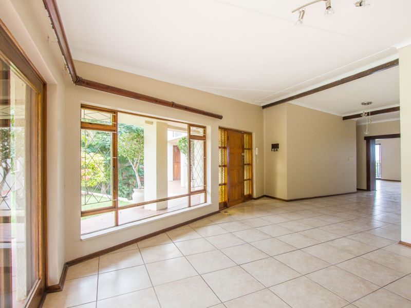 Spacious, empty living area featuring neutral tiled flooring, large wooden-framed windows, and a sliding glass door providing access to the outdoor patio area.