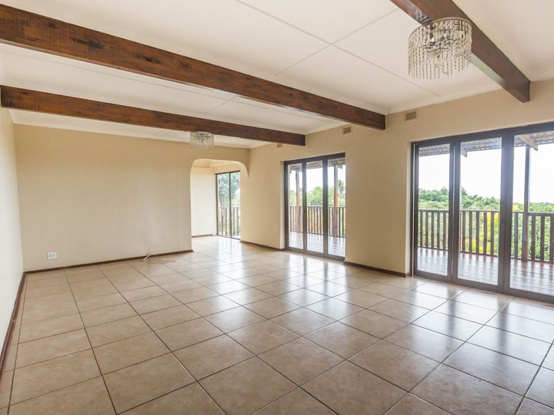 Spacious, light-filled living area featuring exposed timber ceiling beams, ceramic floor tiles, and large sliding doors opening onto a balcony with scenic views.