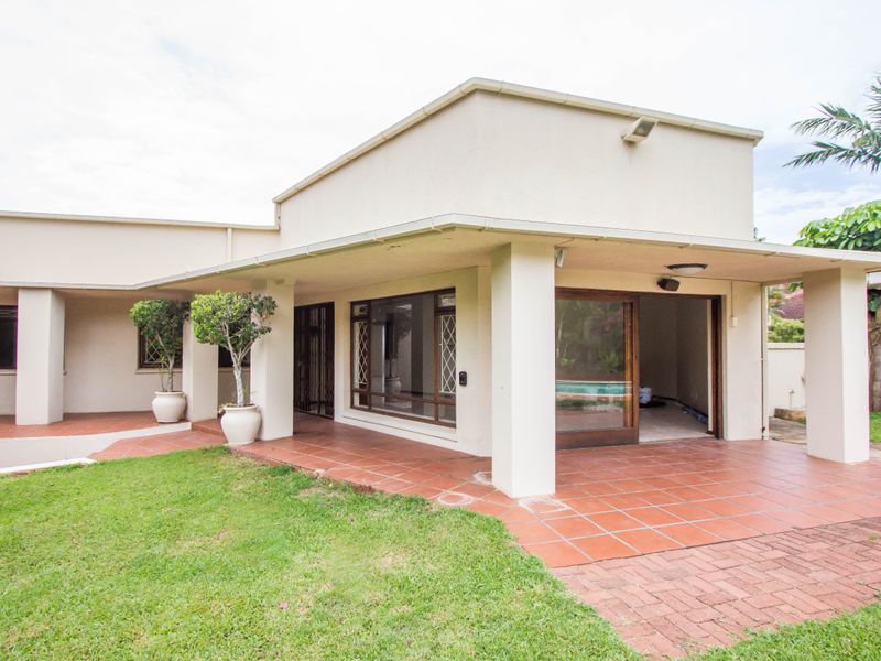 A rear view of the property featuring a covered patio with terracotta tiling, sliding glass doors, and a well-maintained lawn area.