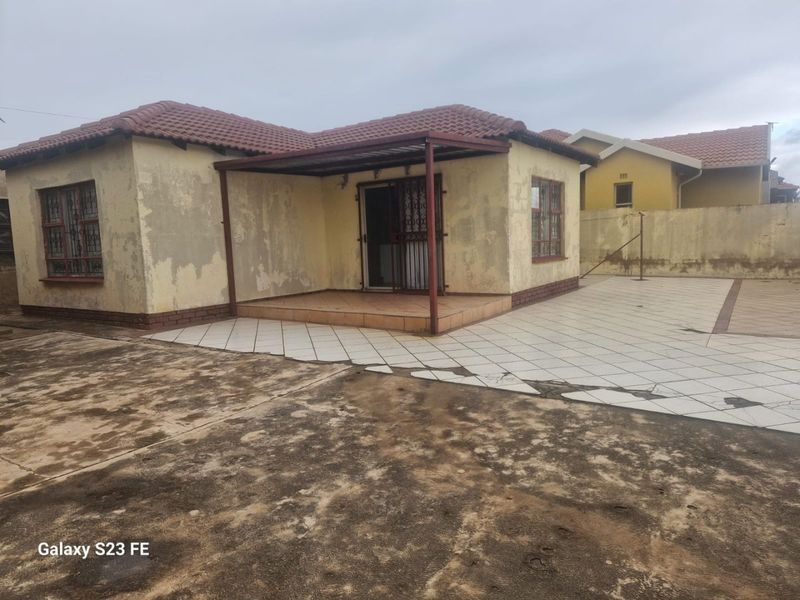 Rear view of a detached house featuring a tiled patio, security gates, and a paved courtyard area requiring exterior maintenance and repainting.