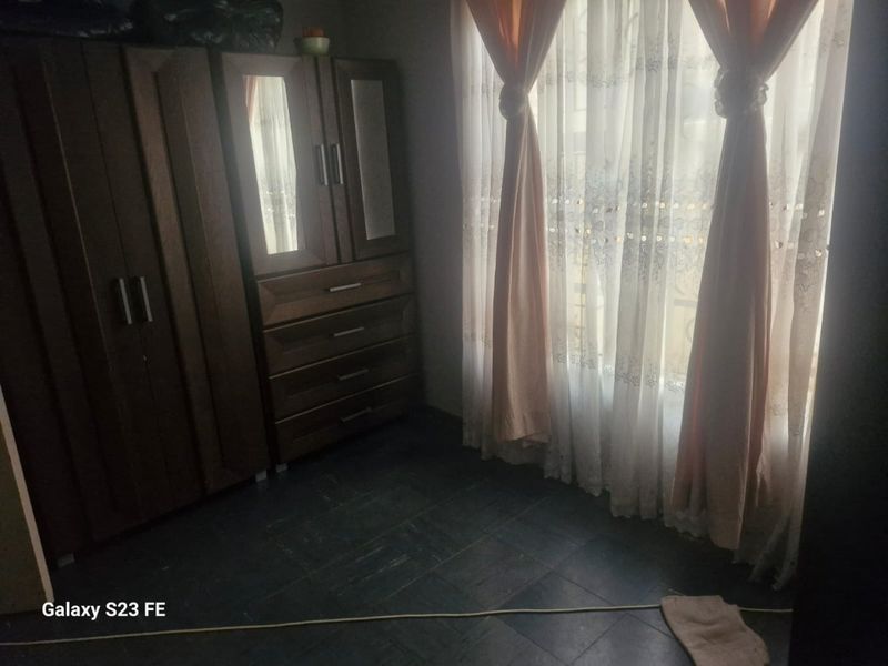 A bedroom featuring dark tiled flooring and natural light filtering through window curtains.