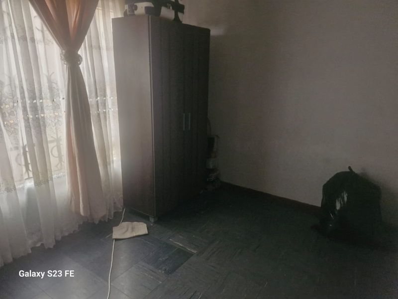 A bedroom featuring dark parquet flooring and natural light from a window, currently requiring cosmetic updates and improved lighting.