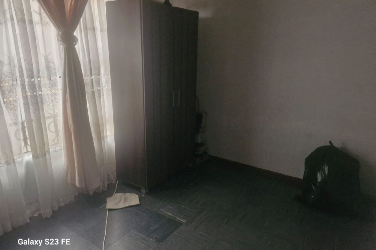 A bedroom featuring dark parquet flooring and natural light from a window, currently requiring cosmetic updates and improved lighting.