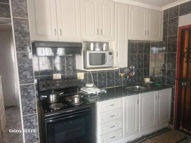 A functional kitchen featuring white cabinetry, dark granite-look countertops, a tiled backsplash, and a freestanding stove with an integrated extractor fan.