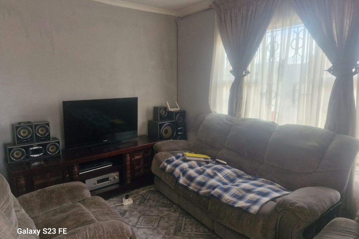 A living room featuring tiled flooring and window security bars, currently showing signs of wear on the wall surfaces.