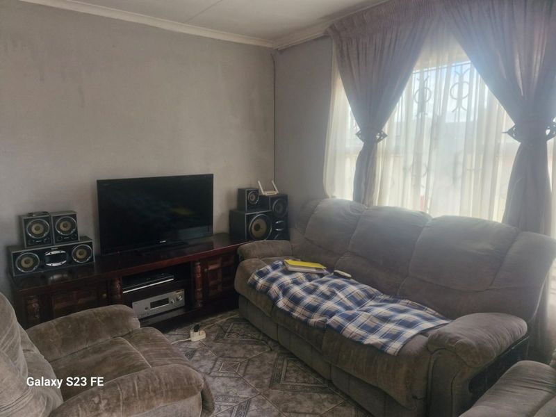 A living room featuring tiled flooring and window security bars, currently showing signs of wear on the wall surfaces.