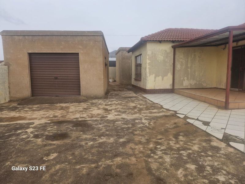 Rear exterior view featuring a detached garage, a covered patio area with tiled flooring, and a concrete driveway requiring maintenance.