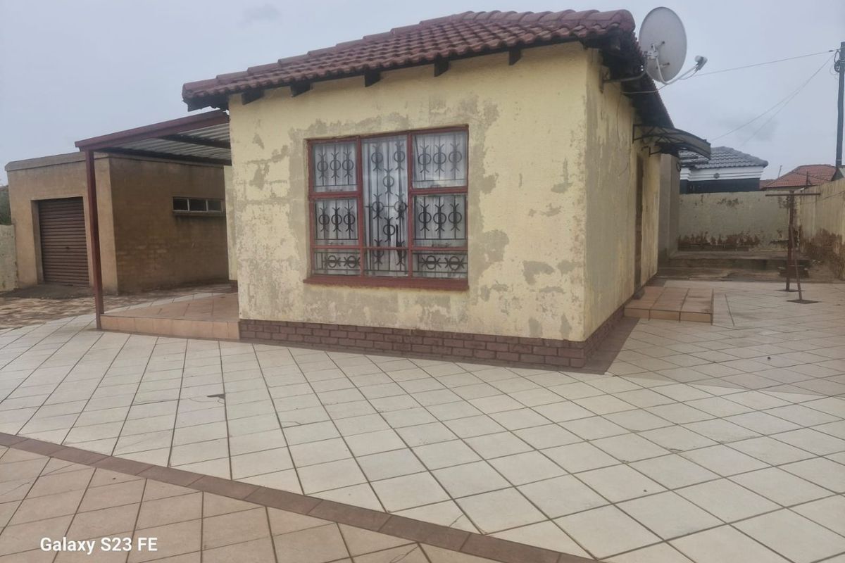 Rear view of the property featuring a tiled patio area, security bars on windows, and a tiled roof structure with visible exterior wall wear.