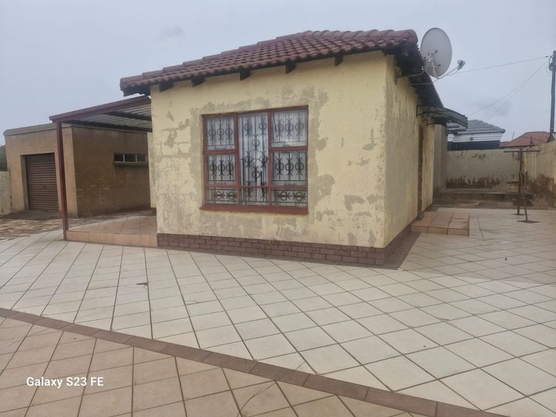 Rear view of the property featuring a tiled patio area, security bars on windows, and a tiled roof structure with visible exterior wall wear.