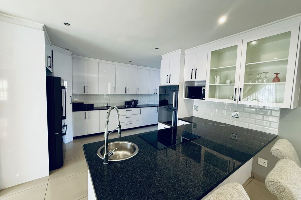 Modern kitchen featuring white cabinetry, black granite countertops, subway tile backsplash, built-in oven, induction cooktop, and a functional island with an undermount sink.