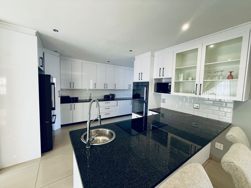 Modern kitchen featuring white cabinetry, black granite countertops, subway tile backsplash, built-in oven, induction cooktop, and a functional island with an undermount sink.