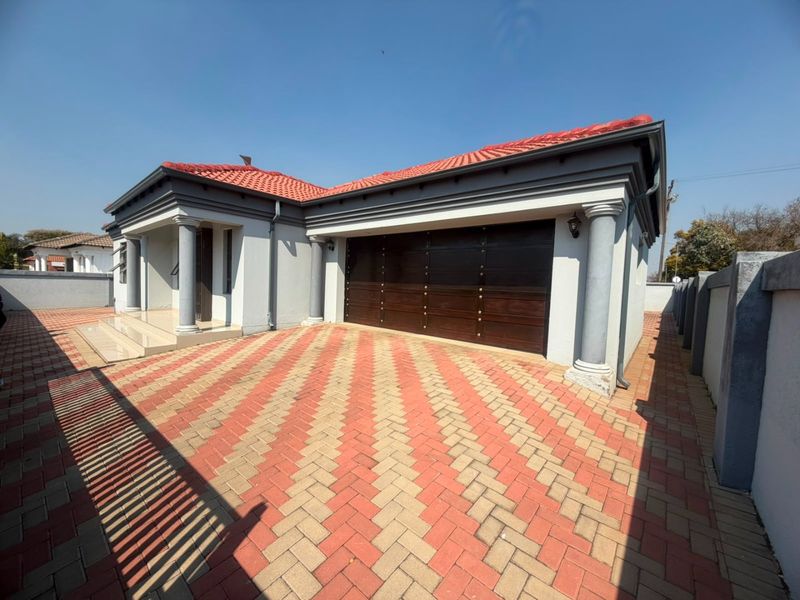 Front view of a well-maintained house featuring a double garage, decorative columns, and a neatly paved driveway with a tiled roof.