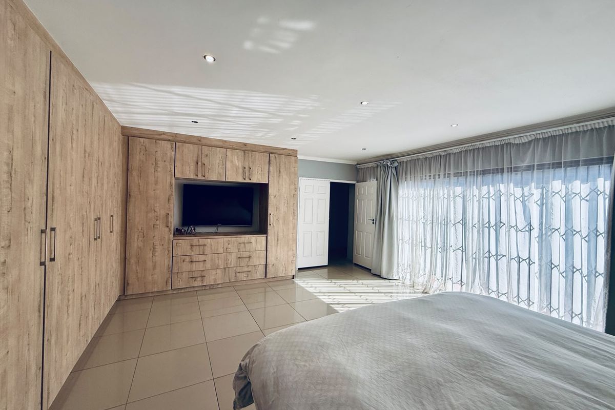 Spacious bedroom featuring extensive built-in wooden cabinetry, tiled flooring, recessed lighting, and large sliding doors leading to an outdoor area with security gates.