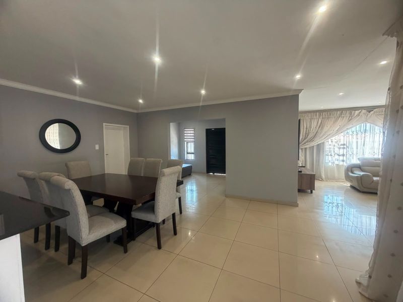 Spacious open-plan living and dining area featuring neutral grey walls, polished porcelain floor tiles, and recessed downlighting throughout.
