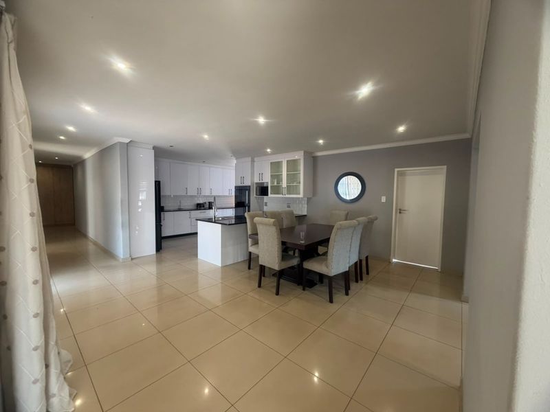 Spacious open-plan living area featuring a modern kitchen with white cabinetry, a central island, and sleek tiled flooring throughout.