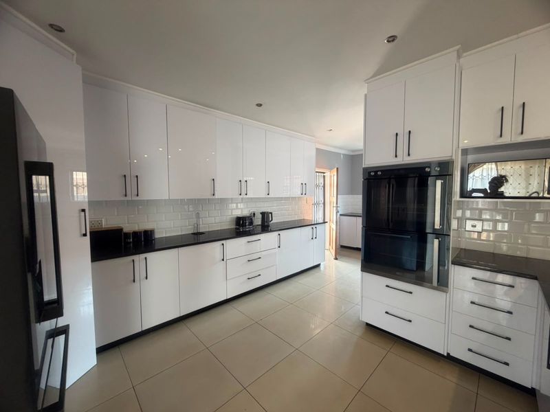 Modern kitchen featuring sleek white cabinetry, black countertops, subway tile backsplash, and integrated double wall ovens with a built-in microwave.