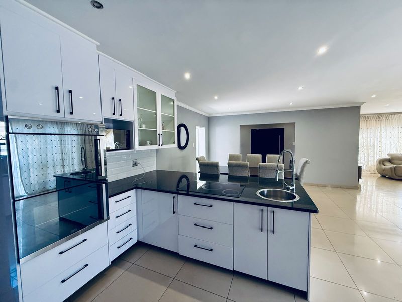 Modern open-plan kitchen featuring high-gloss white cabinetry, dark granite countertops, integrated oven, and sleek tiled flooring, flowing into the dining area.