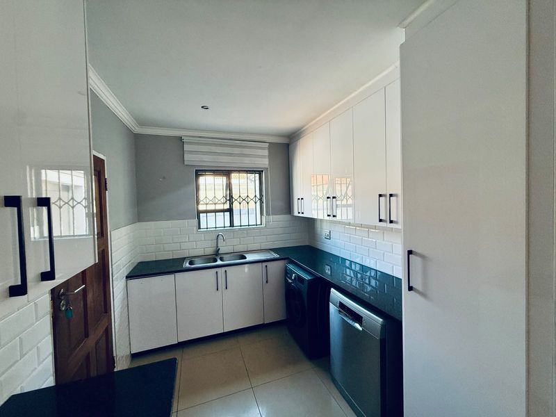 A well-maintained scullery featuring modern white cabinetry, dark stone countertops, subway tile backsplash, and a double basin sink.