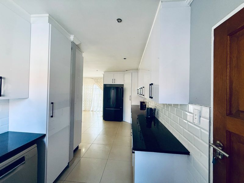 Modern galley-style kitchen featuring sleek white cabinetry, contrasting black granite countertops, subway tile backsplash, and polished floor tiles.