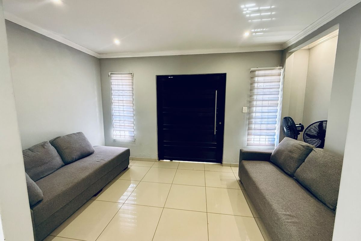 A bright living room featuring neutral tiled flooring, recessed downlighting, and modern roller blinds, providing a clean and functional space.