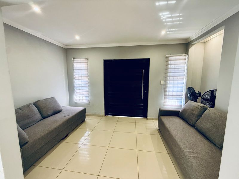 A bright living room featuring neutral tiled flooring, recessed downlighting, and modern roller blinds, providing a clean and functional space.