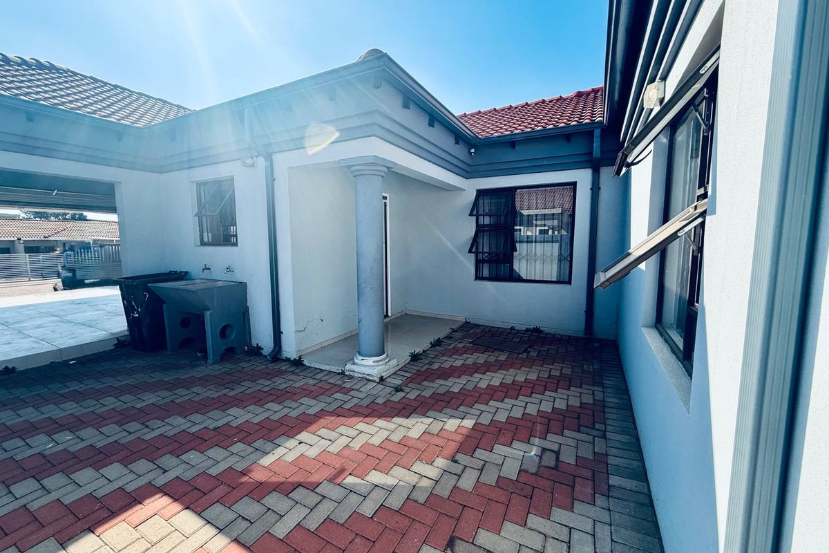 A paved rear courtyard area featuring a covered entrance, structural column, and security-fitted windows, providing a functional outdoor space.