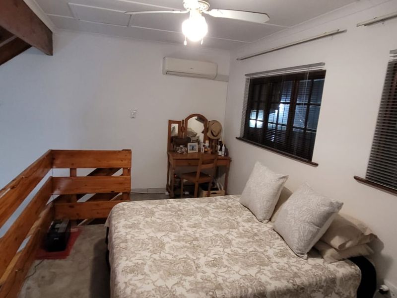 A loft-style bedroom featuring exposed timber rafters, a wooden balustrade, and a split-system air conditioner.